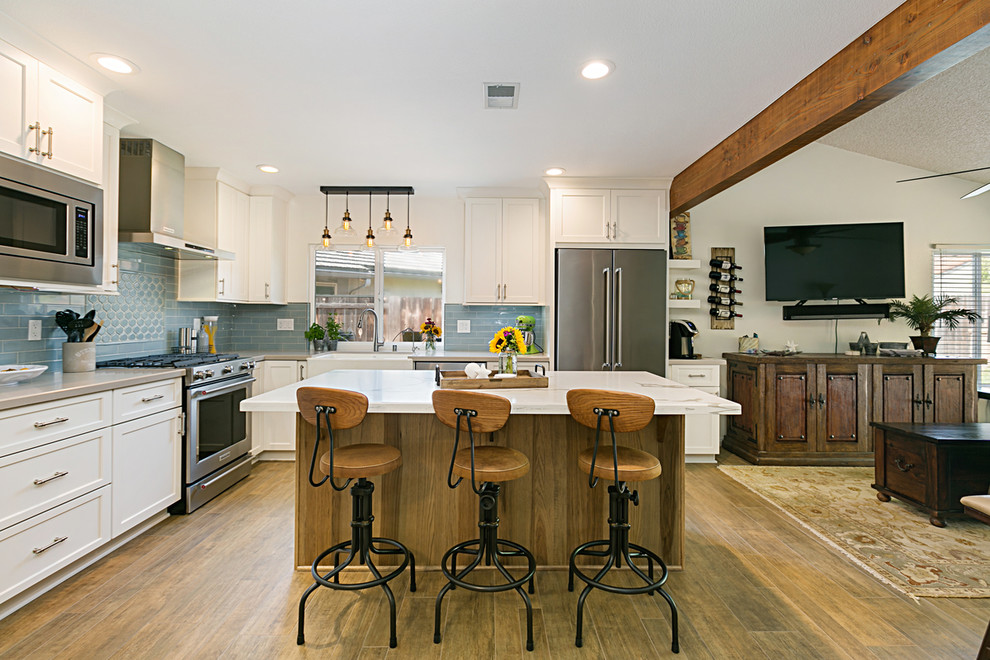 Expansive beach style l-shaped eat-in kitchen in San Diego with a farmhouse sink, recessed-panel cabinets, white cabinets, granite benchtops, blue splashback, subway tile splashback, stainless steel appliances, porcelain floors, with island, brown floor and white benchtop.
