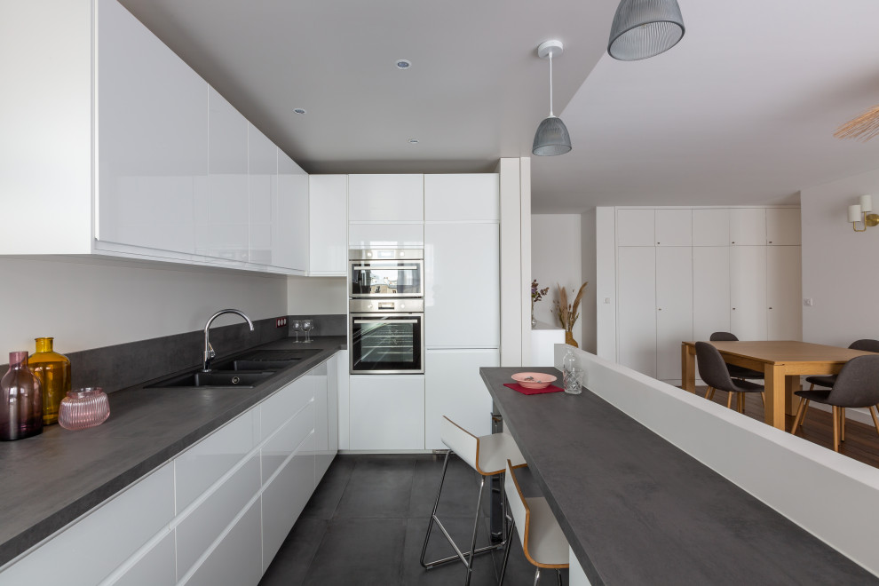 Inspiration for a large contemporary l-shaped eat-in kitchen in Paris with flat-panel cabinets, white cabinets, laminate benchtops, grey splashback, stainless steel appliances, concrete floors, with island, grey benchtop, a double-bowl sink and grey floor.