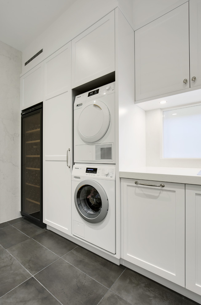 Photo of a mid-sized traditional single-wall utility room in Sydney with shaker cabinets, white cabinets, quartz benchtops, white walls, slate floors, a stacked washer and dryer and grey floor.