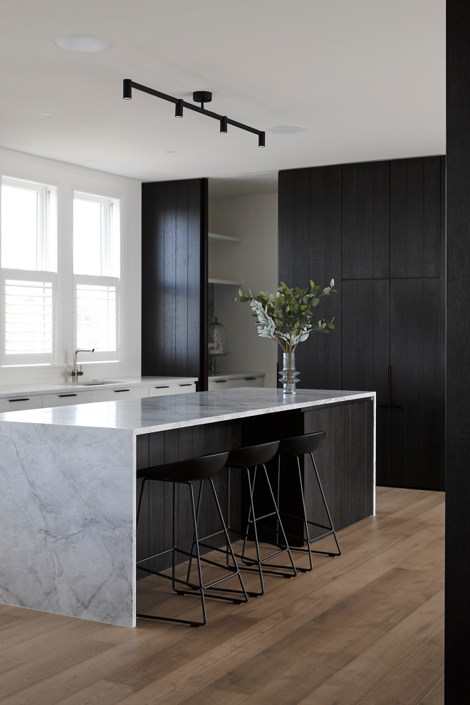 This is an example of a mid-sized modern galley open plan kitchen in Auckland with a drop-in sink, black cabinets, granite benchtops, grey splashback, granite splashback, panelled appliances, dark hardwood floors, with island, brown floor and grey benchtop.