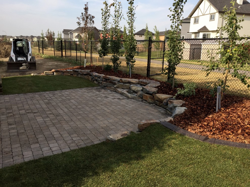 Design ideas for a mid-sized contemporary backyard full sun garden in Edmonton with a retaining wall and natural stone pavers.