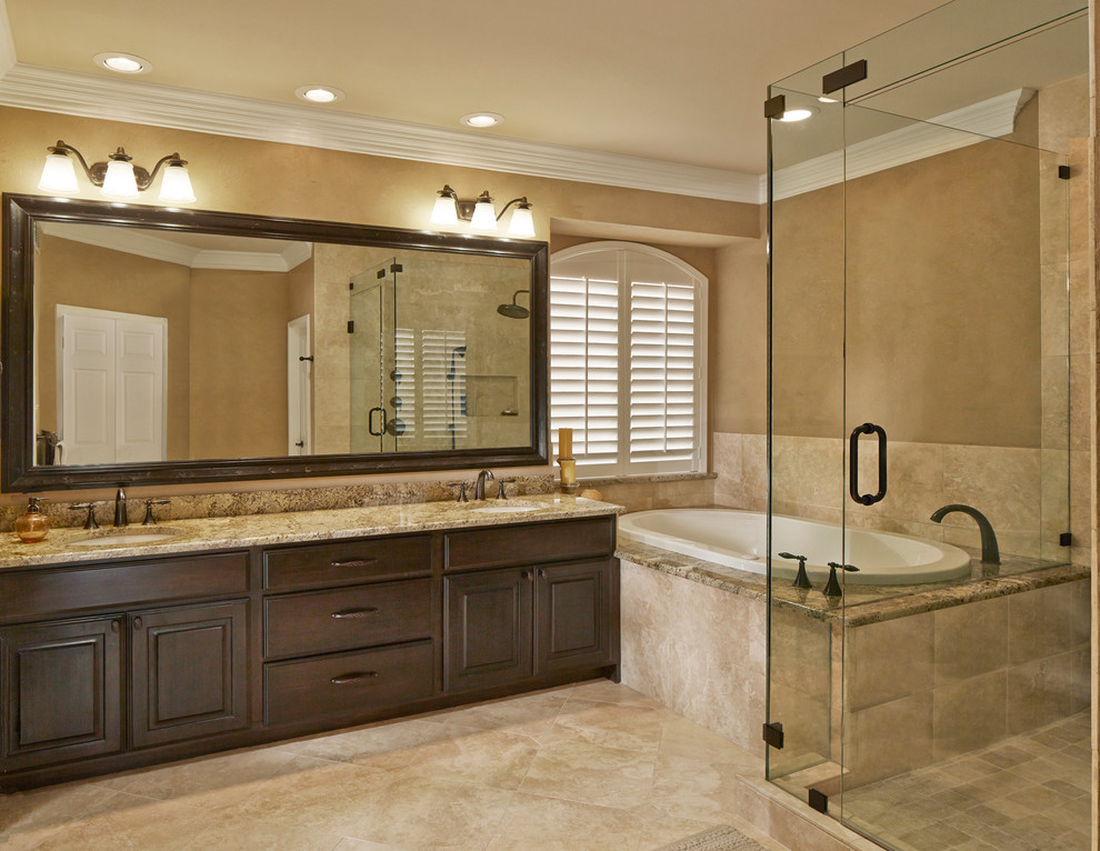 This is an example of a large transitional master bathroom in Dallas with dark wood cabinets, a drop-in tub, beige tile, brown walls, travertine floors, shaker cabinets, a corner shower, an undermount sink, granite benchtops, brown floor and a hinged shower door.