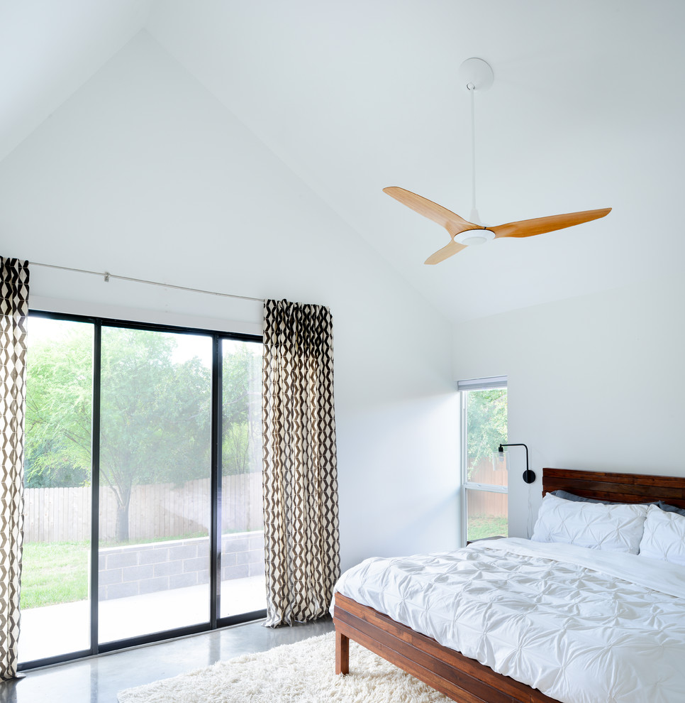 This is an example of a modern master bedroom in Austin with white walls and concrete floors.