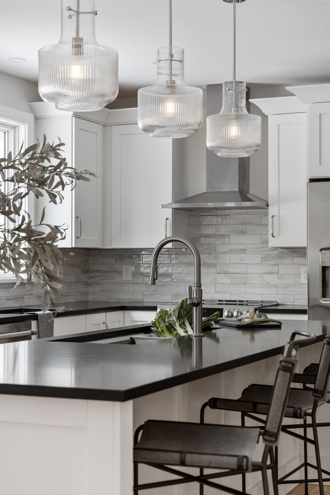 Eat-in kitchen - large transitional u-shaped light wood floor and brown floor eat-in kitchen idea in Burlington with an undermount sink, shaker cabinets, white cabinets, granite countertops, gray backsplash, porcelain backsplash, stainless steel appliances, an island and black countertops