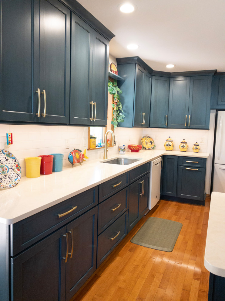 Example of a mid-sized transitional galley light wood floor enclosed kitchen design with an undermount sink, flat-panel cabinets, blue cabinets, quartz countertops, white backsplash, subway tile backsplash, white appliances, a peninsula and white countertops
