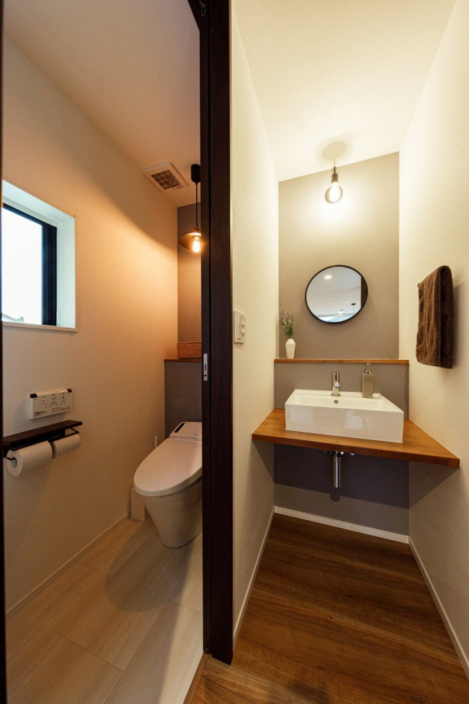 Inspiration för ett mellanstort industriellt brun brunt toalett, med vita skåp, en vägghängd toalettstol, vita väggar, mellanmörkt trägolv, ett fristående handfat och brunt golv