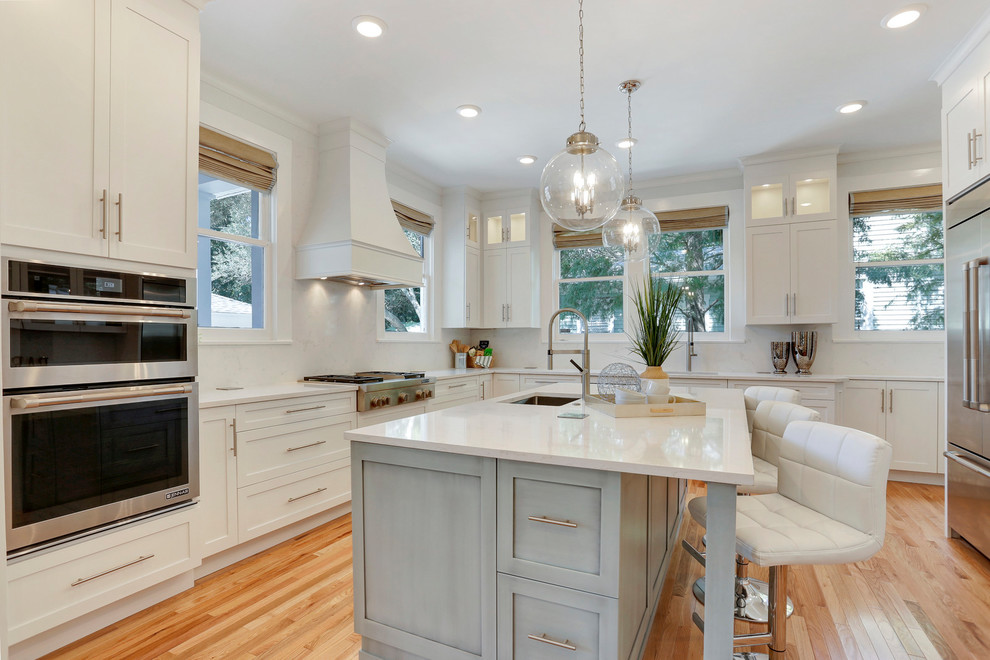Inspiration for a large transitional u-shaped kitchen in Tampa with an undermount sink, shaker cabinets, white cabinets, quartz benchtops, stainless steel appliances, with island, white splashback, stone slab splashback, medium hardwood floors, brown floor and white benchtop.