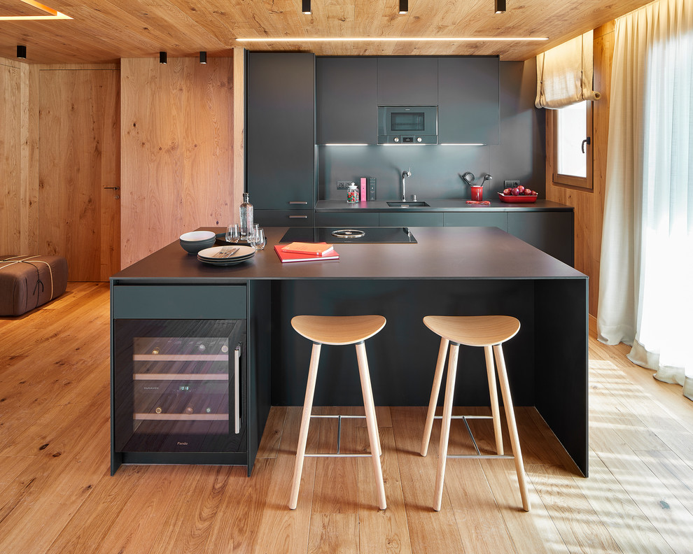 Inspiration for a large modern galley eat-in kitchen in Barcelona with a single-bowl sink, flat-panel cabinets, black cabinets, limestone benchtops, black splashback, limestone splashback, stainless steel appliances, with island, black benchtop, light hardwood floors and beige floor.