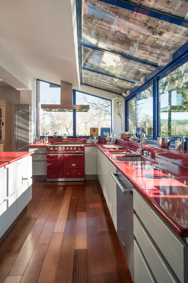 Design ideas for a large midcentury galley eat-in kitchen in Marseille with a double-bowl sink, flat-panel cabinets, grey cabinets, solid surface benchtops, red splashback, panelled appliances, medium hardwood floors, with island, brown floor and red benchtop.