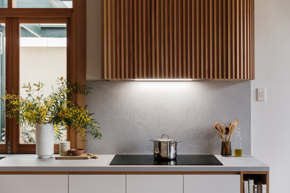 Mid-sized midcentury l-shaped eat-in kitchen in Adelaide with an undermount sink, flat-panel cabinets, black cabinets, solid surface benchtops, grey splashback, stone slab splashback, panelled appliances, light hardwood floors, with island, brown floor and grey benchtop.