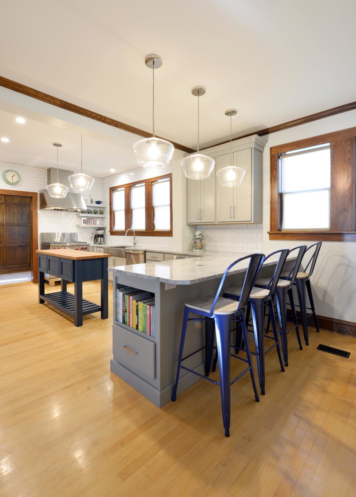Inspiration for a mid-sized transitional light wood floor and brown floor enclosed kitchen remodel with a farmhouse sink, shaker cabinets, gray cabinets, wood countertops, white backsplash, porcelain backsplash, stainless steel appliances, an island and brown countertops