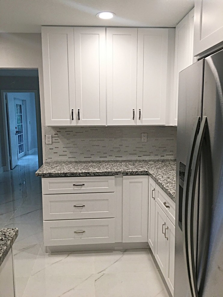 Inspiration for a small transitional l-shaped open plan kitchen in Miami with an undermount sink, shaker cabinets, white cabinets, granite benchtops, white splashback, metal splashback, stainless steel appliances, porcelain floors, with island and white floor.