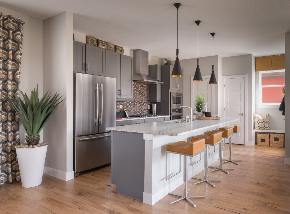 Inspiration for a transitional galley medium tone wood floor and brown floor kitchen remodel with an undermount sink, shaker cabinets, gray cabinets, brown backsplash, mosaic tile backsplash, stainless steel appliances, an island and white countertops