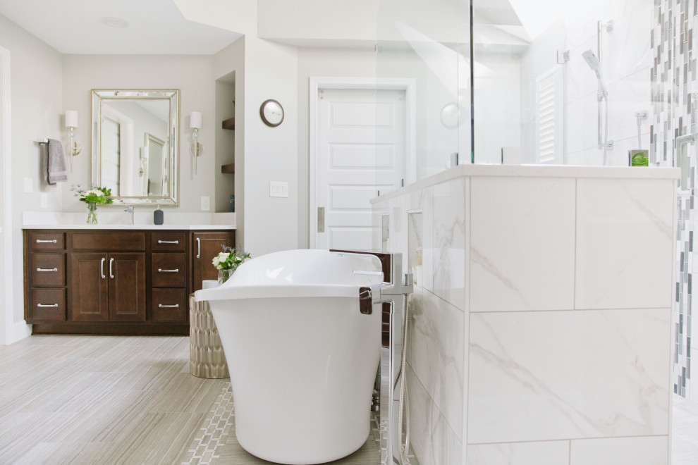 This is an example of a large transitional master bathroom in Seattle with beaded inset cabinets, dark wood cabinets, a freestanding tub, a double shower, a one-piece toilet, white tile, porcelain tile, grey walls, porcelain floors, an undermount sink, engineered quartz benchtops, grey floor, a hinged shower door and white benchtops.