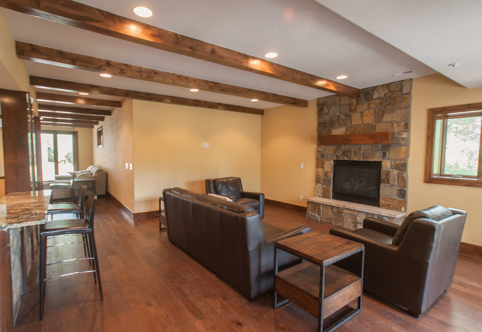 Photo of a large country walk-out basement in Denver with yellow walls, dark hardwood floors, a standard fireplace and a stone fireplace surround.