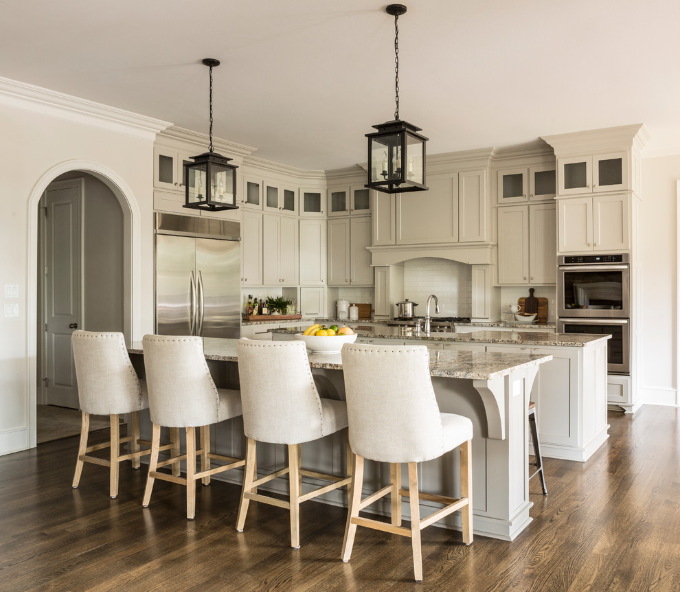 This is an example of a transitional l-shaped kitchen in Little Rock with shaker cabinets, grey cabinets, white splashback, subway tile splashback, stainless steel appliances, dark hardwood floors and multiple islands.