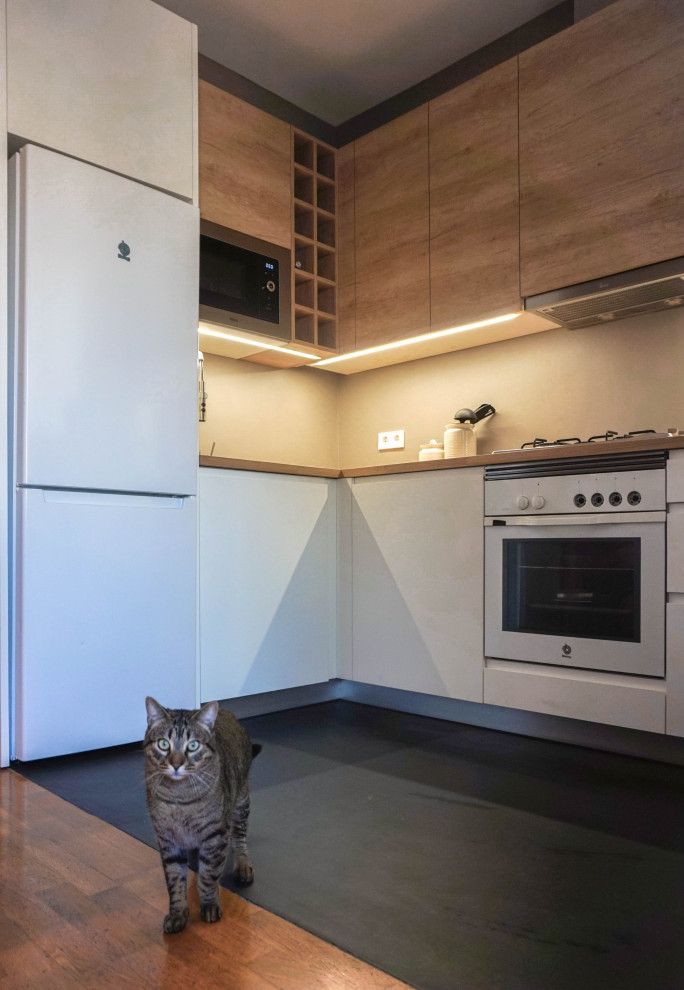 Photo of a small scandinavian l-shaped open plan kitchen in Barcelona with a single-bowl sink, flat-panel cabinets, medium wood cabinets, wood benchtops, grey splashback, cement tile splashback, white appliances, concrete floors, no island, black floor and beige benchtop.