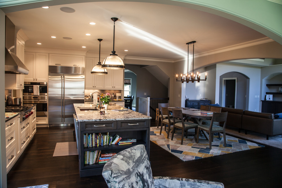 Example of a transitional dark wood floor and brown floor open concept kitchen design with an undermount sink, shaker cabinets, white cabinets, granite countertops, beige backsplash, subway tile backsplash, stainless steel appliances and an island