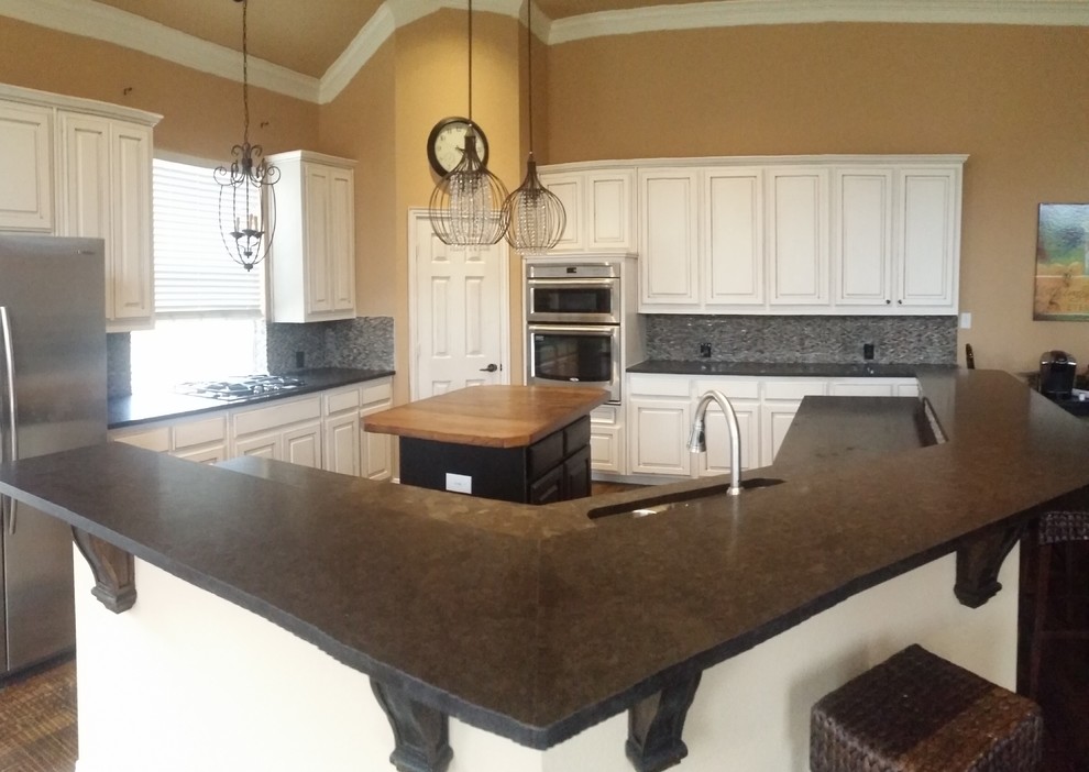 Example of a large transitional brown floor open concept kitchen design in Dallas with an undermount sink, raised-panel cabinets, white cabinets, granite countertops, gray backsplash, stone tile backsplash, stainless steel appliances and an island