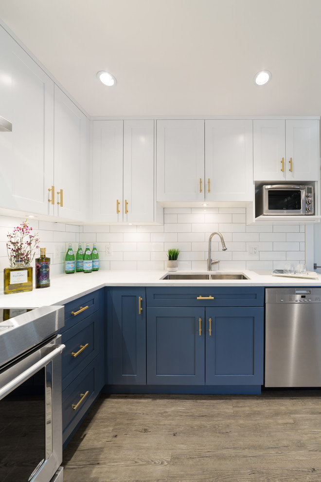 Design ideas for a mid-sized country eat-in kitchen in Vancouver with a double-bowl sink, recessed-panel cabinets, blue cabinets, solid surface benchtops, white splashback, subway tile splashback, stainless steel appliances, vinyl floors and with island.