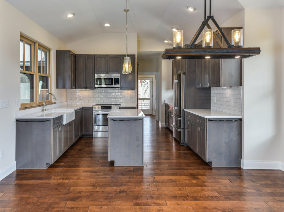Small country l-shaped open plan kitchen in Other with a farmhouse sink, recessed-panel cabinets, distressed cabinets, quartzite benchtops, white splashback, subway tile splashback, stainless steel appliances, medium hardwood floors, with island and brown floor.