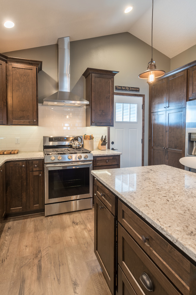 This is an example of a large country u-shaped separate kitchen in Minneapolis with a double-bowl sink, shaker cabinets, dark wood cabinets, granite benchtops, white splashback, subway tile splashback, stainless steel appliances, dark hardwood floors, with island and brown floor.