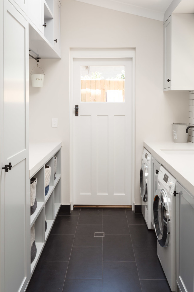 This is an example of a small beach style galley dedicated laundry room in Sydney with white cabinets, white walls, a side-by-side washer and dryer, black floor and shaker cabinets.