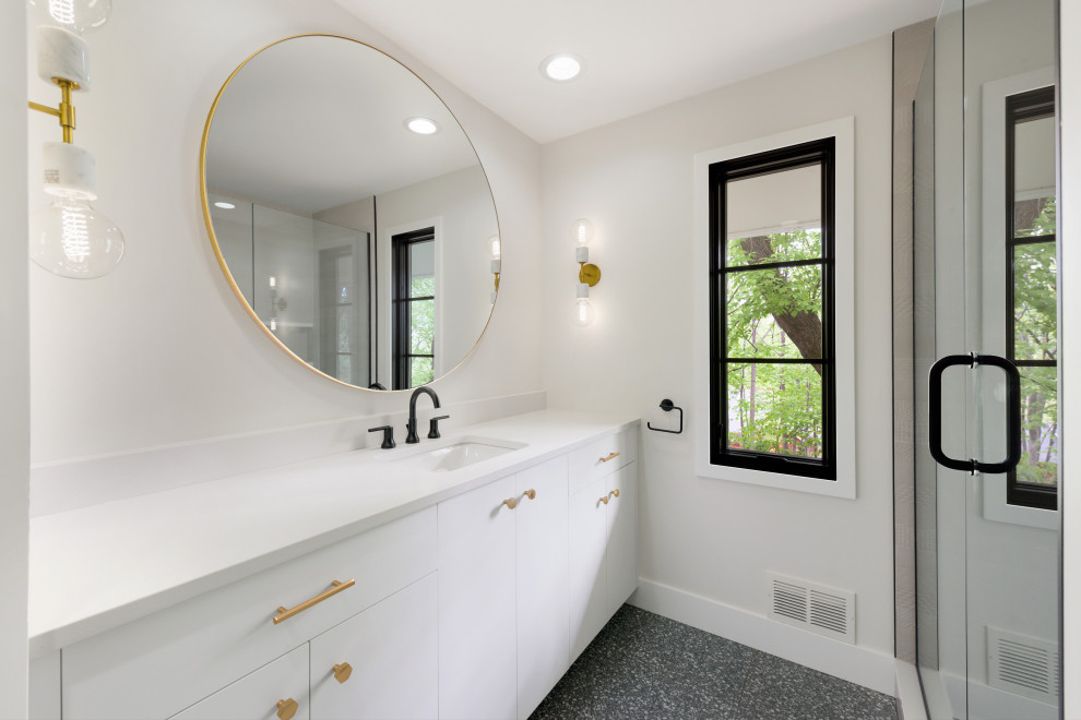 Photo of a large midcentury kids bathroom in Minneapolis with flat-panel cabinets, blue cabinets, an alcove shower, a one-piece toilet, white walls, terrazzo floors, an undermount sink, engineered quartz benchtops, black floor, a hinged shower door and white benchtops.