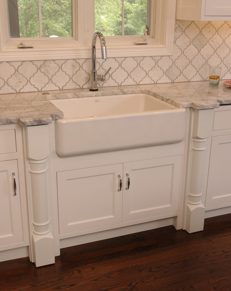This is an example of a large country u-shaped eat-in kitchen in Cincinnati with a farmhouse sink, white cabinets, white splashback, stainless steel appliances, dark hardwood floors, with island, marble benchtops, marble splashback, beaded inset cabinets and brown floor.