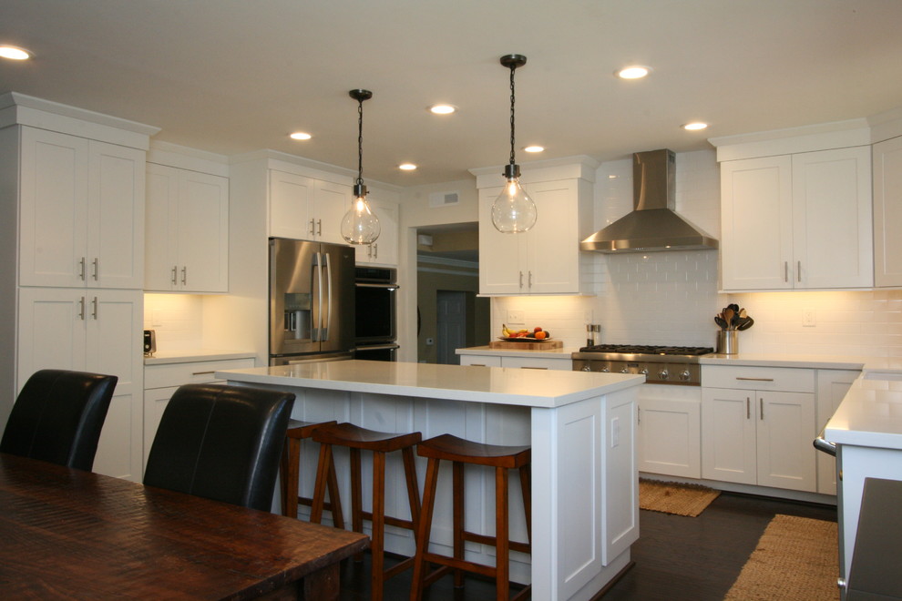 Example of a large transitional u-shaped dark wood floor eat-in kitchen design in Orange County with a farmhouse sink, shaker cabinets, white cabinets, quartz countertops, white backsplash, ceramic backsplash, stainless steel appliances and an island