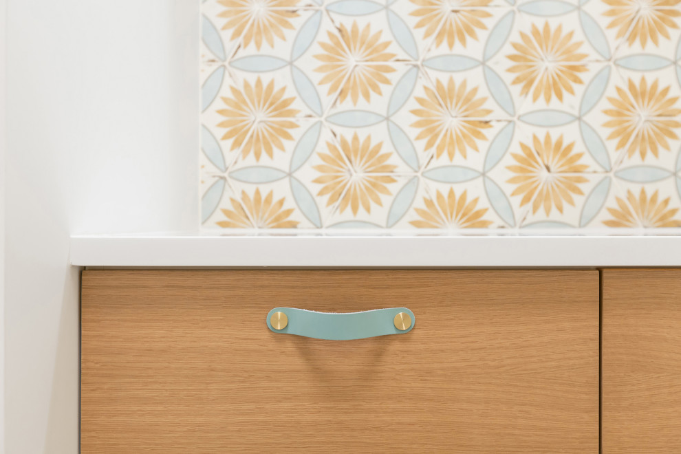 Minimalist single-wall light wood floor and brown floor utility room photo in Indianapolis with flat-panel cabinets, medium tone wood cabinets, multicolored backsplash, white walls, a stacked washer/dryer, white countertops, quartz countertops and porcelain backsplash