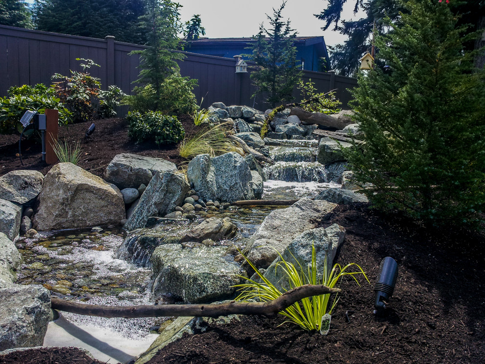 Photo of a mid-sized rustic full sun backyard stone water fountain landscape in Seattle for spring.