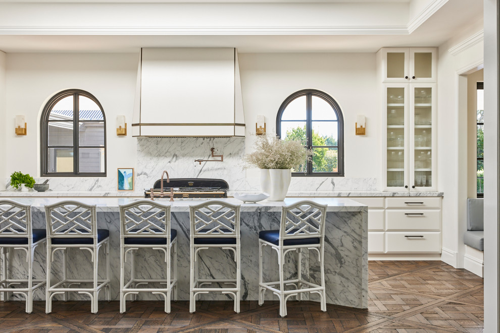 Photo of a transitional galley kitchen in Other with white cabinets, medium hardwood floors, with island, brown floor, white benchtop, recessed, flat-panel cabinets, white splashback and black appliances.