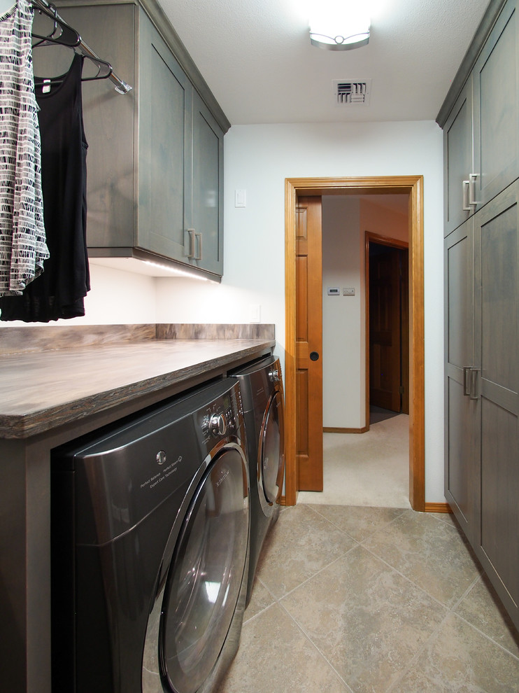 This is an example of a mid-sized transitional galley dedicated laundry room in Seattle with an undermount sink, recessed-panel cabinets, dark wood cabinets, solid surface benchtops, blue walls, porcelain floors, a side-by-side washer and dryer, brown splashback, beige floor and brown benchtop.
