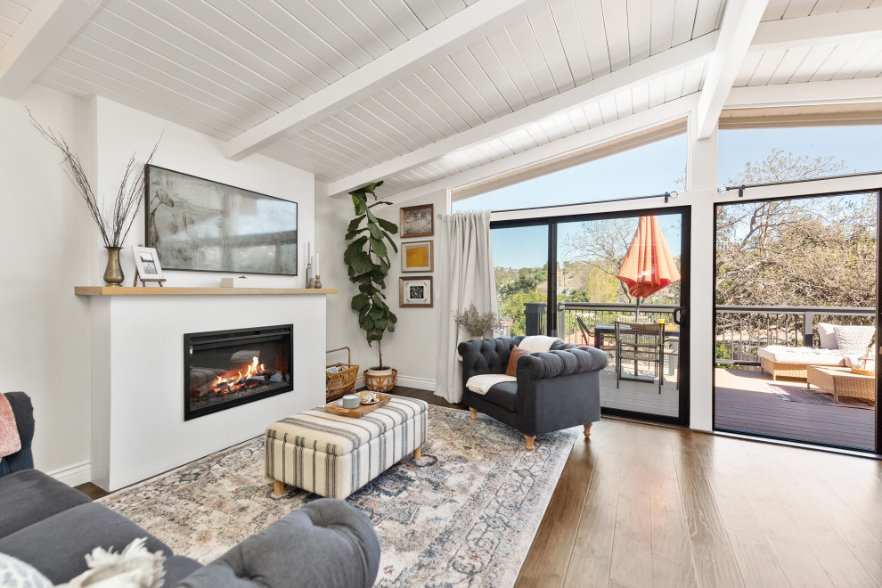 Photo of a small midcentury open concept family room in Los Angeles with white walls, light hardwood floors, a standard fireplace, a plaster fireplace surround, a freestanding tv, beige floor and vaulted.