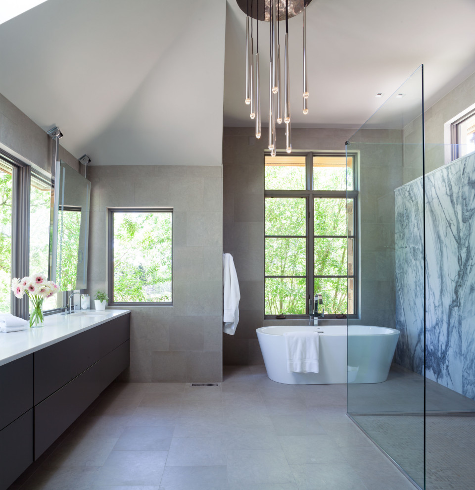 Photo of a large contemporary master bathroom in Denver with flat-panel cabinets, grey cabinets, a freestanding tub, a curbless shower, a wall-mount toilet, gray tile, limestone, white walls, limestone floors, an undermount sink, engineered quartz benchtops, grey floor, a hinged shower door, white benchtops, a shower seat, a double vanity, a floating vanity and vaulted.