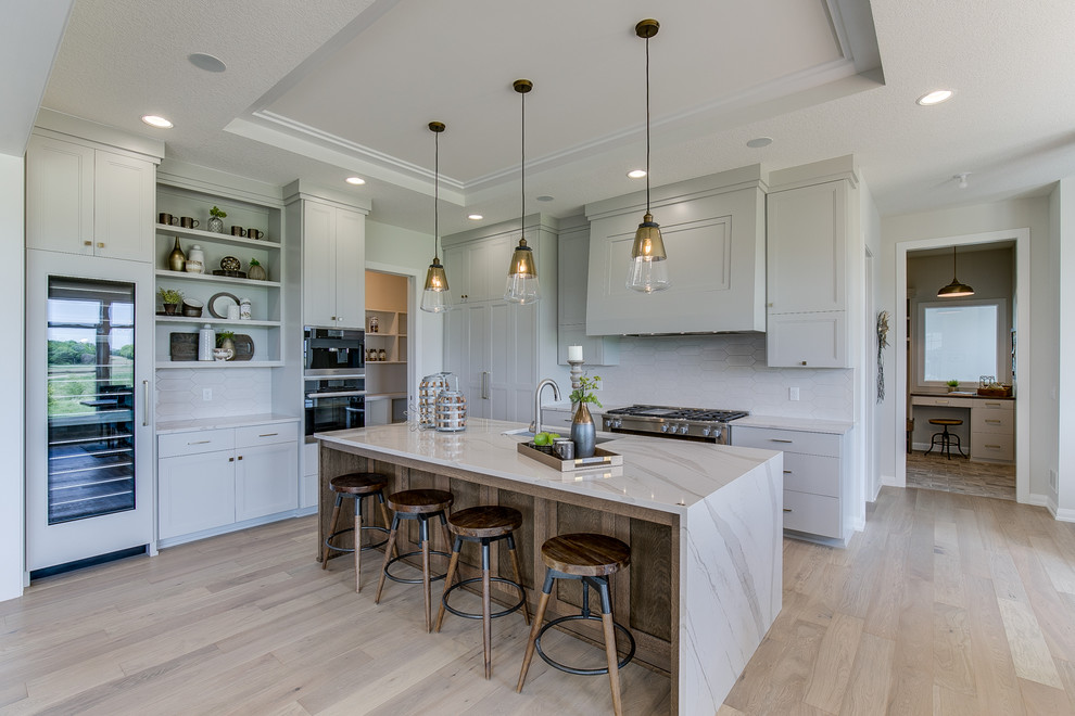Transitional u-shaped kitchen in Minneapolis with shaker cabinets, grey cabinets, white splashback, stainless steel appliances, medium hardwood floors, with island, brown floor and white benchtop.
