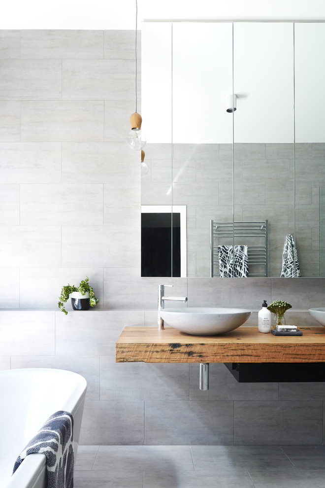 Photo of a modern master bathroom in Melbourne with a freestanding tub, gray tile, grey walls, ceramic floors, a vessel sink, wood benchtops, grey floor and brown benchtops.