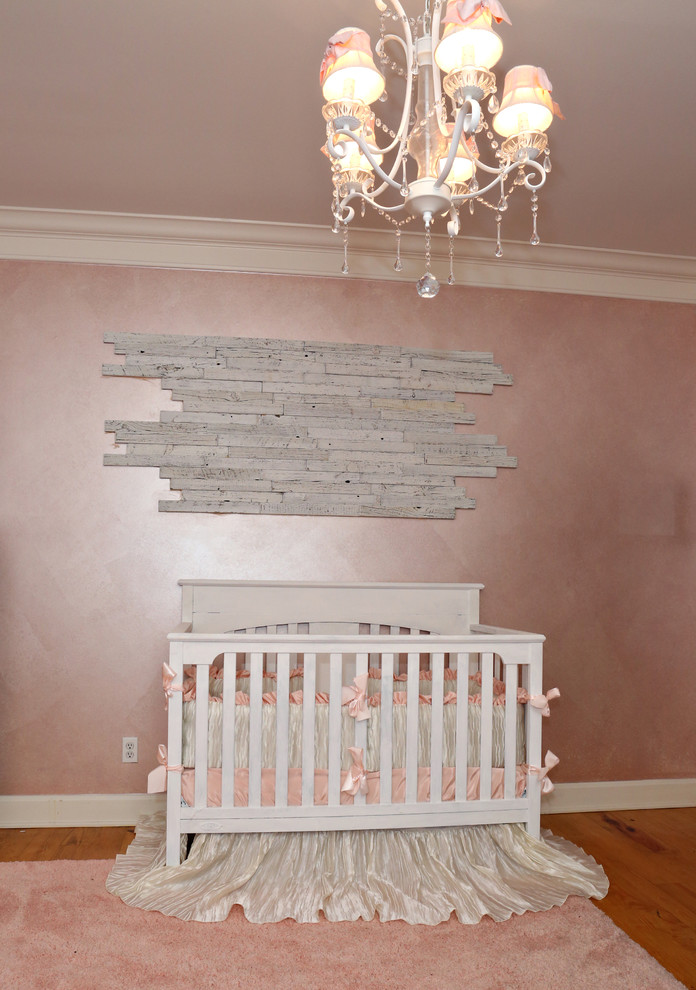 Design ideas for a mid-sized traditional nursery for girls in Louisville with pink walls and light hardwood floors.