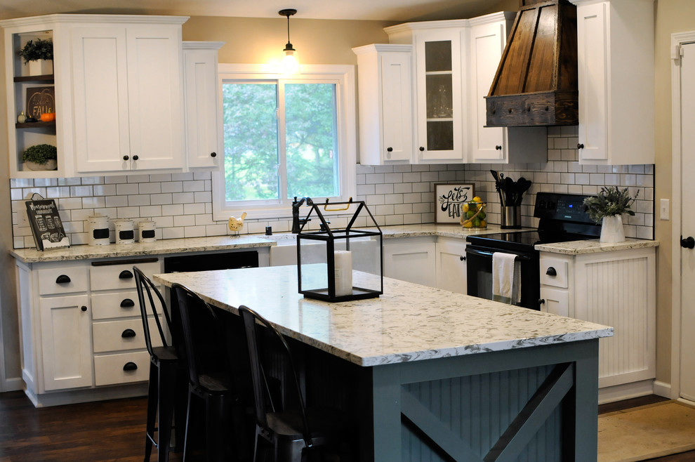 Large country l-shaped eat-in kitchen in Minneapolis with a farmhouse sink, shaker cabinets, white cabinets, quartz benchtops, white splashback, subway tile splashback, black appliances, dark hardwood floors, with island, brown floor and white benchtop.