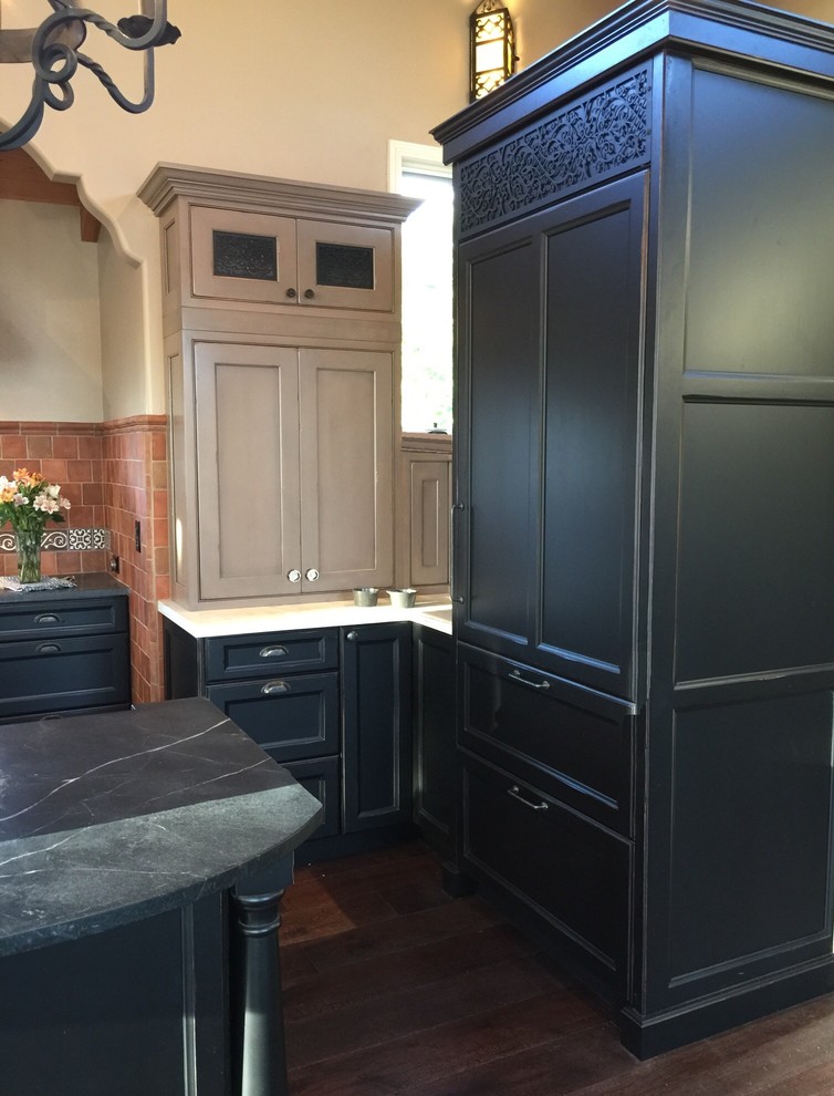 This is an example of a mid-sized traditional galley open plan kitchen in San Diego with a farmhouse sink, recessed-panel cabinets, distressed cabinets, soapstone benchtops, multi-coloured splashback, terra-cotta splashback, stainless steel appliances, dark hardwood floors and with island.