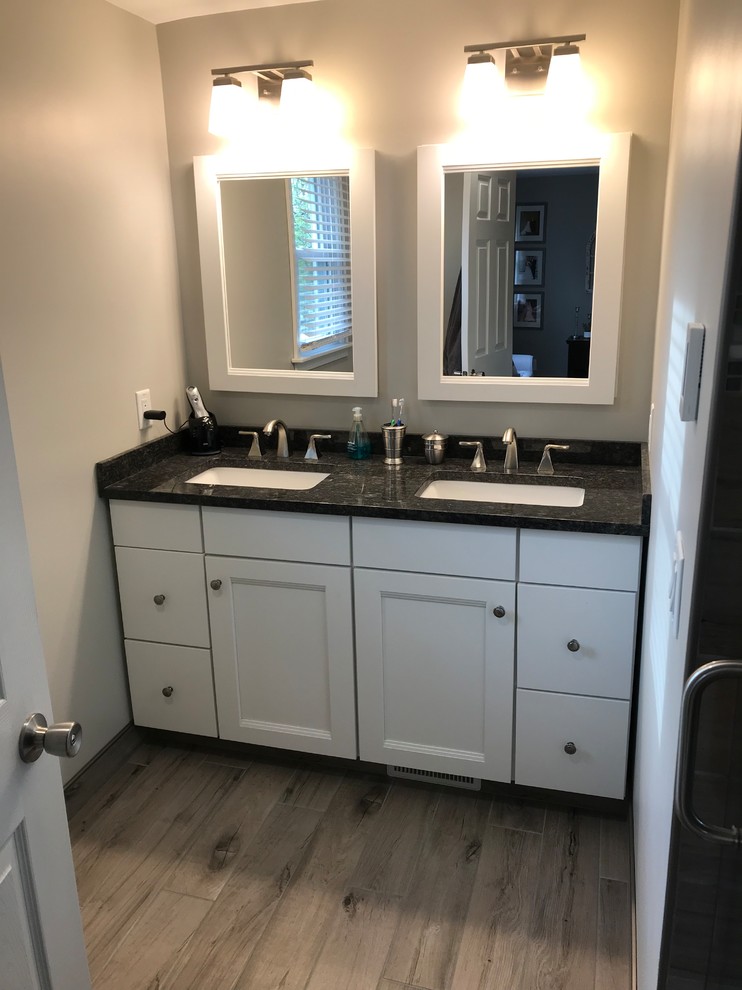 Photo of a small contemporary master wet room bathroom in New York with flat-panel cabinets, white cabinets, gray tile, ceramic tile, beige walls, ceramic floors, an undermount sink, granite benchtops, grey floor, a hinged shower door and black benchtops.