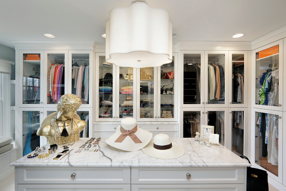 This is an example of a large traditional women's dressing room in Chicago with glass-front cabinets, white cabinets and carpet.