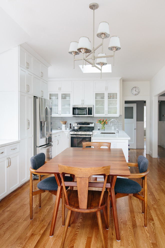 This is an example of a transitional u-shaped eat-in kitchen in San Francisco with an undermount sink, shaker cabinets, white cabinets, grey splashback, subway tile splashback, stainless steel appliances, medium hardwood floors and a peninsula.