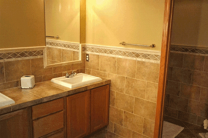 This is an example of a traditional bathroom in Minneapolis with a drop-in sink, white cabinets, an alcove shower, brown tile, ceramic tile and ceramic floors.