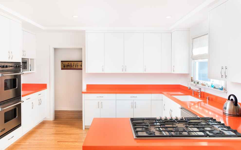 サンフランシスコにあるミッドセンチュリースタイルのおしゃれなコの字型キッチン (アンダーカウンターシンク、フラットパネル扉のキャビネット、白いキャビネット、シルバーの調理設備、淡色無垢フローリング、オレンジのキッチンカウンター) の写真