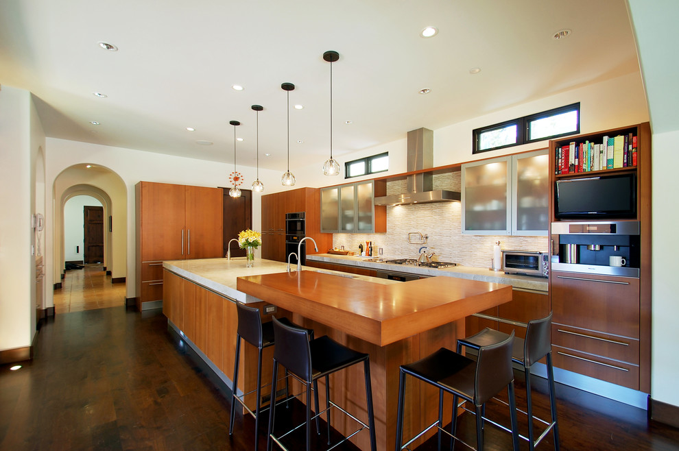Photo of a mediterranean l-shaped eat-in kitchen in Los Angeles with wood benchtops, an undermount sink, flat-panel cabinets, medium wood cabinets, beige splashback, matchstick tile splashback, stainless steel appliances, medium hardwood floors and with island.