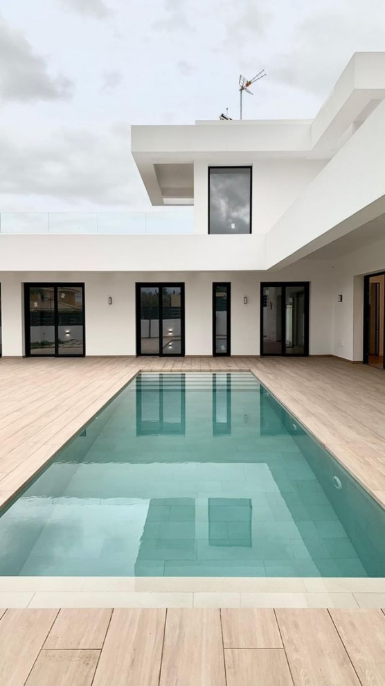 Modelo de piscina alargada minimalista grande rectangular en patio con paisajismo de piscina y suelo de baldosas