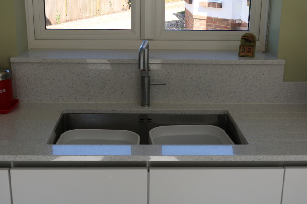 This is an example of a mid-sized modern eat-in kitchen in Sussex with an undermount sink, flat-panel cabinets, white cabinets, quartzite benchtops, red splashback, glass sheet splashback, black appliances, a peninsula and grey benchtop.