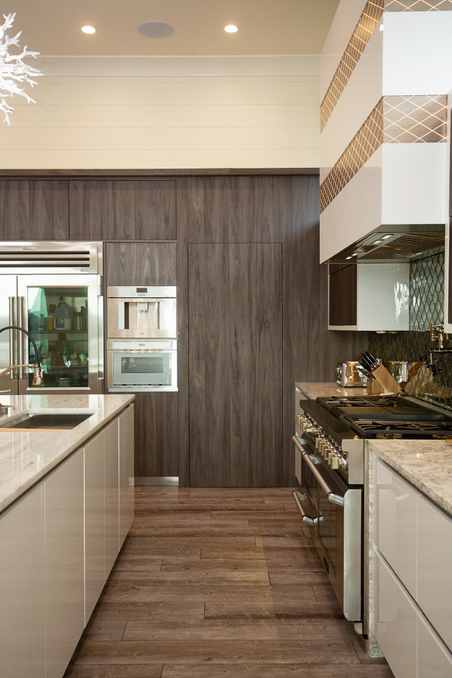 Large modern l-shaped kitchen/diner in Miami with a built-in sink, flat-panel cabinets, metallic splashback, glass tiled splashback, stainless steel appliances, medium hardwood flooring, an island, brown floors and white worktops.